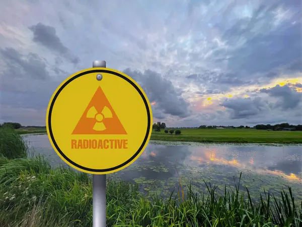 Radioactive pollution. Yellow warning sign with hazard symbol near lake