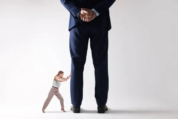 Small woman pushing giant man on light background