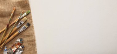 Doğal çuval bezi kumaşı ve beyaz arka planda farklı boya malzemeleri, üst manzara. Metin için boşluk