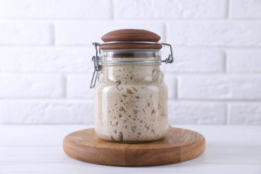 Sourdough starter in glass jar on white wooden table clipart