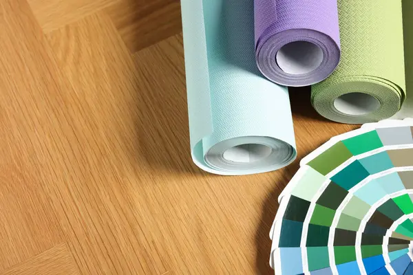 Different wallpaper rolls and color palette samples on wooden table, space for text