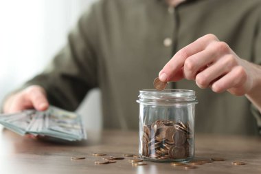 Finansal tasarruflar. Ahşap masada cam kavanoza bozuk para koyan adam, yakın plan.