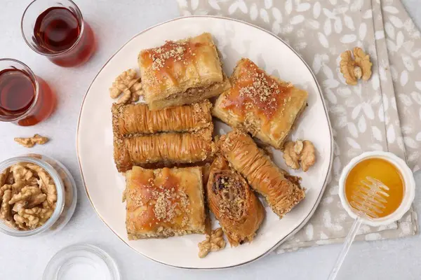 Eastern sweets. Pieces of tasty baklava, honey and tea on white table, flat lay