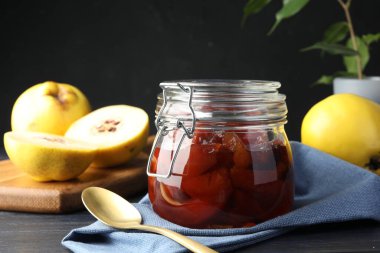 Ayva reçeli cam kavanozda, kaşık ve taze çiğ meyveler gri masada, yakın plan.