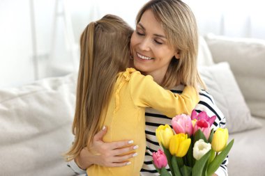 Evde anneler günüyle annesini tebrik eden küçük bir kız. Bir buket güzel lale tutan bir kadın.