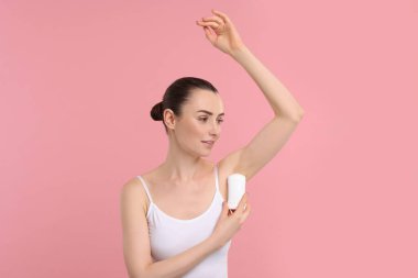 Güzel bir kadın pembe arka plana deodorant sürüyor.