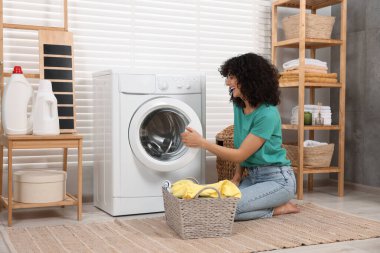 Çamaşır makinesinin yanında çamaşırları olan mutlu kadın.
