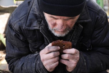 Zavallı evsiz adam elinde bir parça ekmek tutuyor.