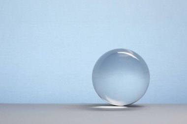 Masanın üzerinde açık mavi arka plana karşı şeffaf cam top. Metin için boşluk