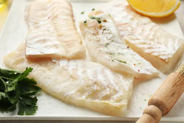 Fresh raw cod fillets with spices and brush on plate, closeup