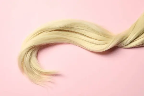 Blonde hair strand on pink background, top view