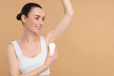 Güzel bir kadın bej arkaplan üzerine deodorant sürüyor, metin için boşluk