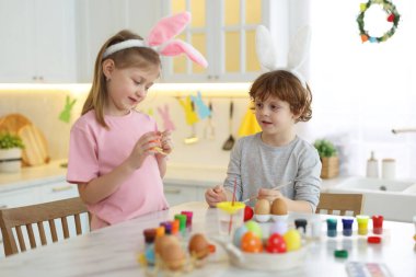 Paskalya kutlaması. Tavşan kulaklı şirin çocuklar mutfaktaki beyaz mermer masada yumurta boyuyorlar.