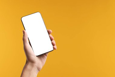 Sarı arka planda boş ekranlı akıllı telefon tutan adam, yakın plan. Tasarım için model