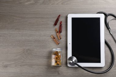 Modern tablet, steteskop, ampuller ve tahta masa üzerinde haplar, düz yatak. Metin için boşluk