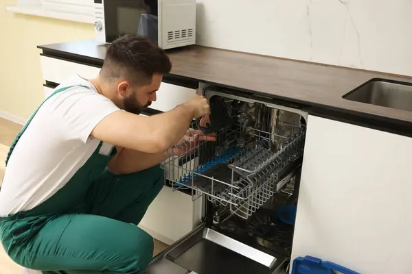 Serviceman examining dishwasher cutlery rack in kitchen