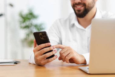 Ofisteki ahşap masada akıllı telefon kullanan genç adam, yakın plan.