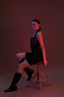 Neon ışıklarda arka planda taburede poz veren güzel genç bir kadın.