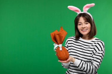 Paskalya kutlaması. Tavşan kulaklı mutlu kadın ve yeşil arka plana sarılı yumurta, mesaj için yer