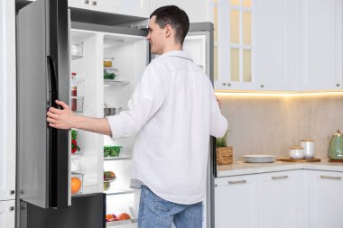 Buzdolabının yanında mutlu bir adam var. Mutfakta, arka tarafta.