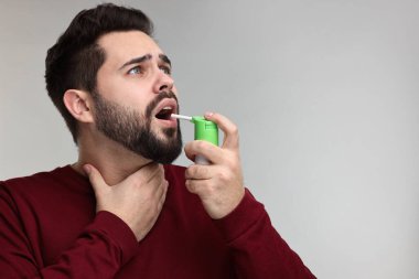 Gri arka planda boğaz spreyi kullanan genç bir adam. Metin için boşluk