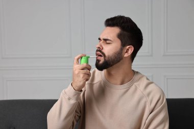 Genç adam evde boğaz spreyi kullanıyor.