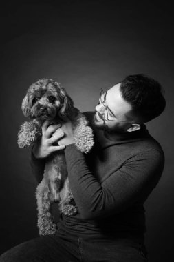 Siyah arka planda sevimli köpeği olan yakışıklı sakallı adam. Siyah ve beyaz etkisi