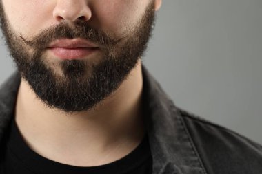 Gri arka planda bıyıklı yakışıklı genç adam, yakın plan.