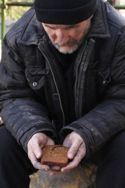 Zavallı evsiz adam elinde bir parça ekmek tutuyor.