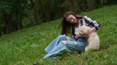 Parktaki yeşil çimlerde dinlenen sevimli köpeğiyle bir kadın.