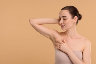 Güzel bir kadın bej arka planda pürüzsüz ciltli koltukaltını gösteriyor.