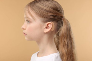 Soluk kahverengi arka planda işitme cihazı olan küçük kız.