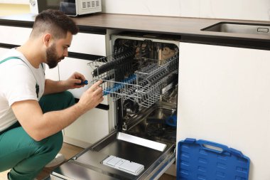 Görevli mutfakta bulaşık makinesini tornavidayla tamir ediyor.