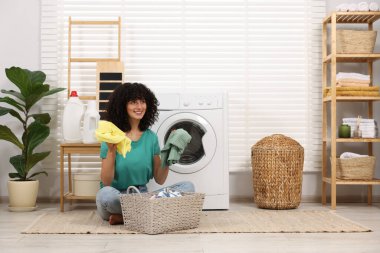 Çamaşır makinesinin yanında çamaşırları olan mutlu kadın.