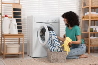 Çamaşır makinesine çamaşır koyan mutlu bir kadın.