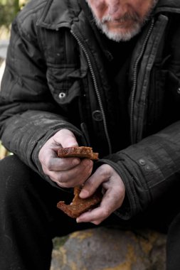 Zavallı evsiz adam elinde bir parça ekmek tutuyor.