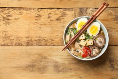 Bir kase lezzetli ramen ve yemek çubukları ahşap masada, üst manzarada yazı için yer var. Erişte çorbası.