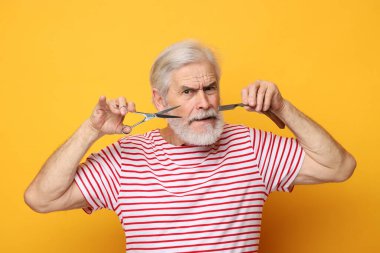 Bıyıklı yaşlı adam elinde makas ve turuncu arka planda bıçak tutuyor.
