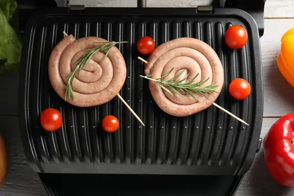 Electric grill with homemade sausages, rosemary and vegetables on rustic wooden table, flat lay