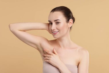 Güzel bir kadın bej arka planda pürüzsüz, temiz bir ciltle koltukaltı gösteriyor.