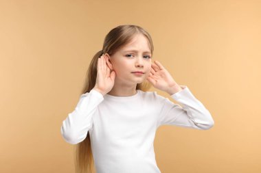 Soluk kahverengi arka planda işitme sorunu olan küçük bir kız.