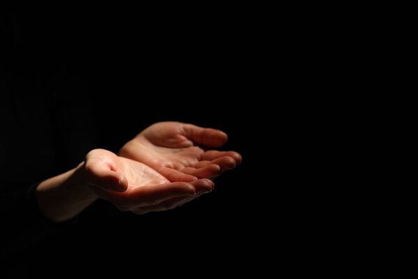 Religion. Woman with open palms praying on black background, closeup. Space for text