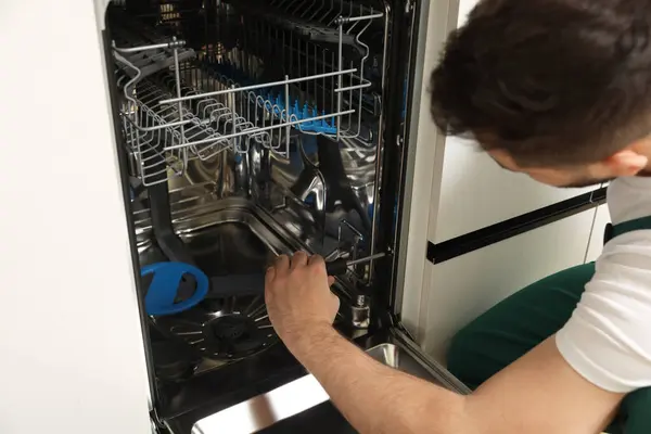 Serviceman repairing dishwasher with screwdriver indoors, closeup