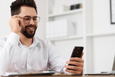 Ofisteki masada akıllı telefon kullanan yakışıklı genç adam.