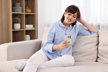 Evdeki kanepede akıllı telefon kullanan güzel bir ev hanımı.