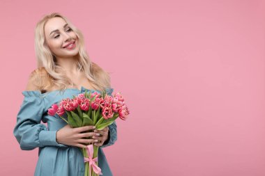 Tozlu pembe arka planda güzel bir buketi olan mutlu genç kadın. Metin için boşluk