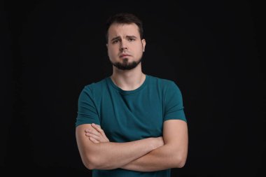Siyah arka planda çapraz kollu üzgün bir adamın portresi.