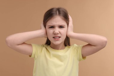 İşitme problemi. Soluk kahverengi arka planda kulak ağrısı çeken küçük bir kız.