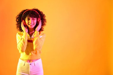 Güzel, genç bir kadın kulaklıkla müzik dinliyor. Renkli arka planda, neon ışıklarla. Metin için boşluk