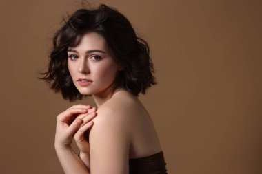 Kahverengi arka planda dalgalı saç stili olan güzel bir genç kadının portresi. Metin için boşluk